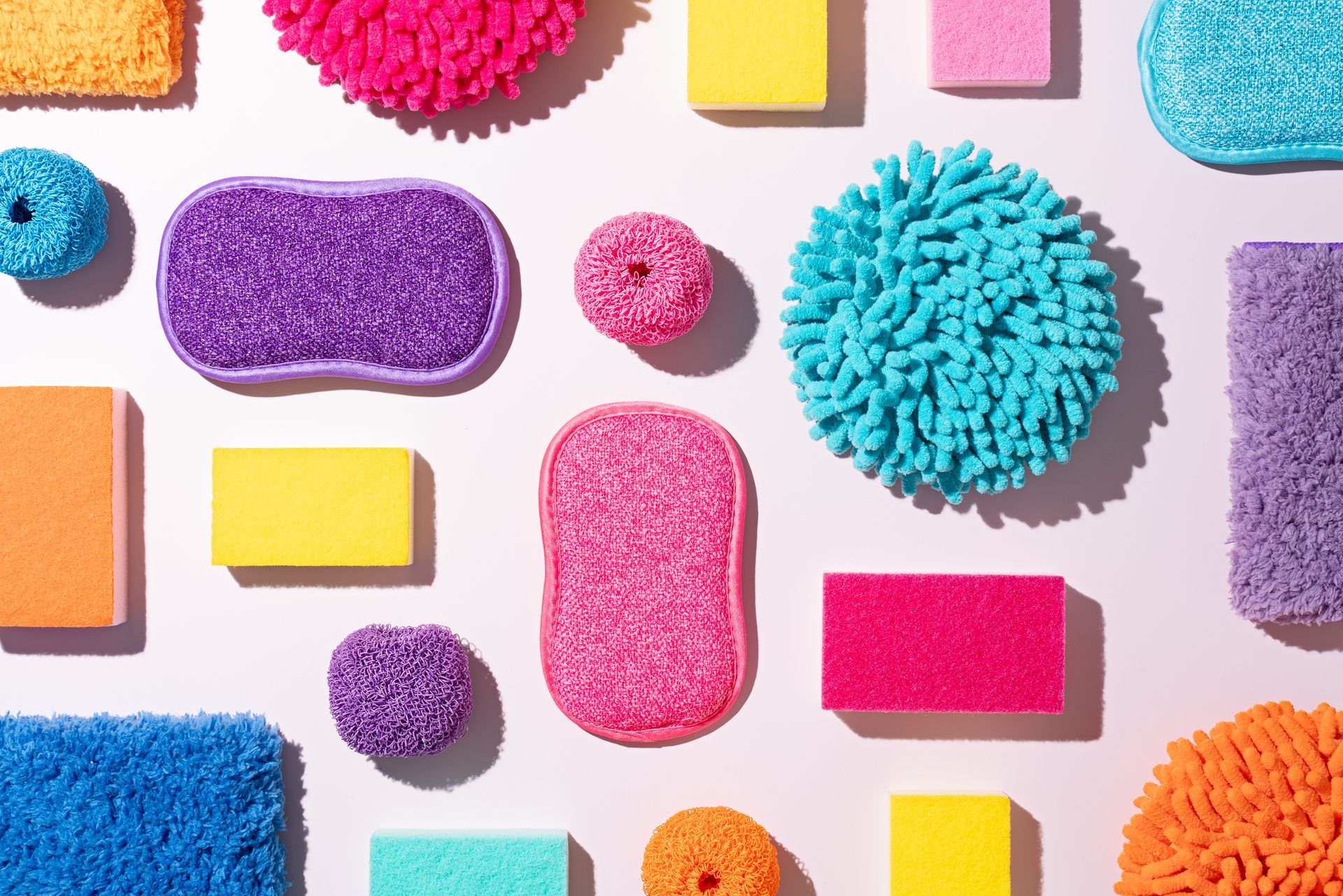 Colorful sponges arranged on a white background, various shapes and textures, including rectangular and round.