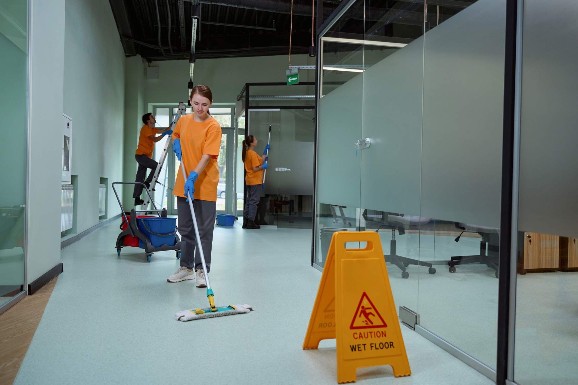 A cleaner using a mop to wash the floor beside a caution sign, showcasing commercial cleaning