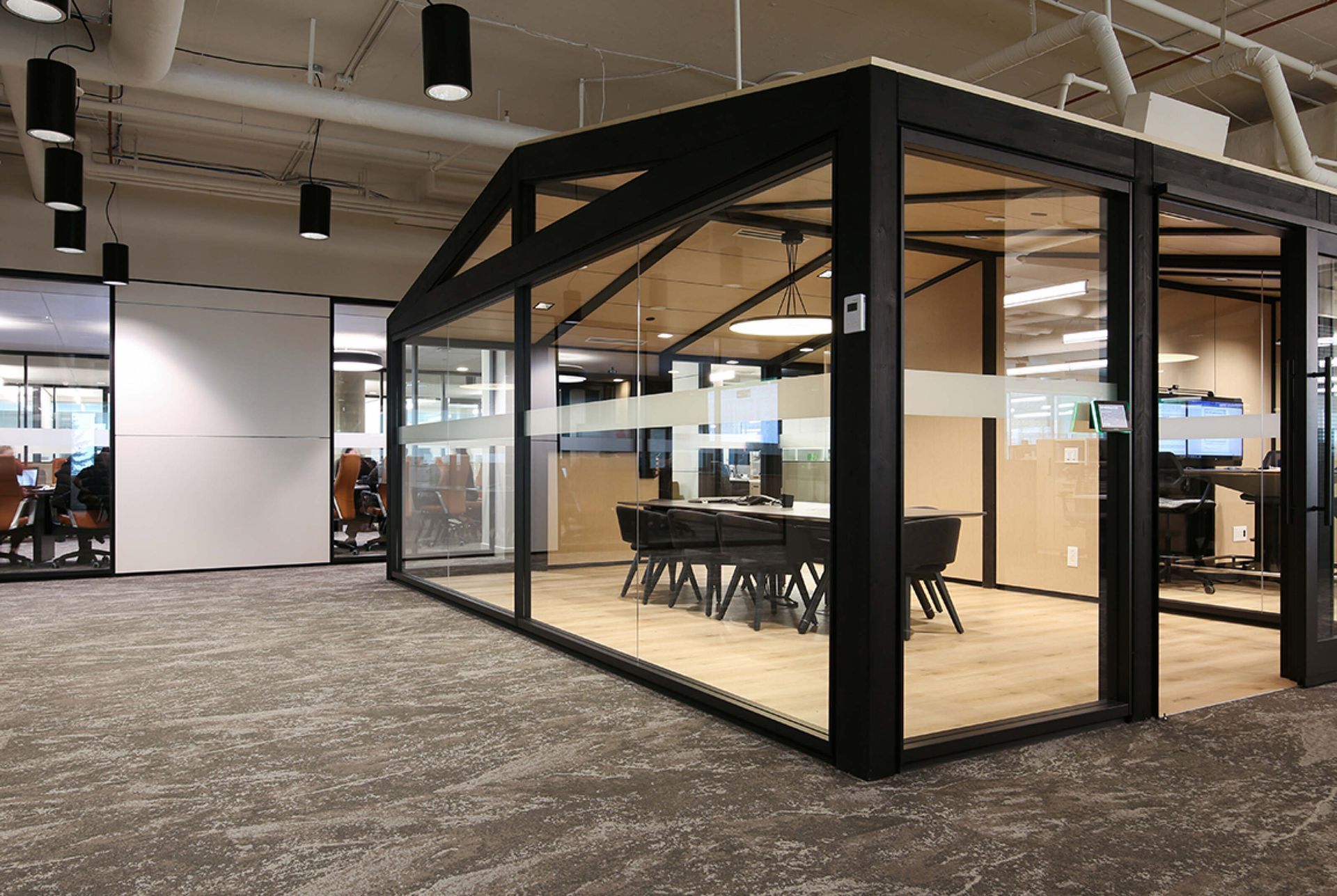 Glass meeting pod with black frame in an open office space