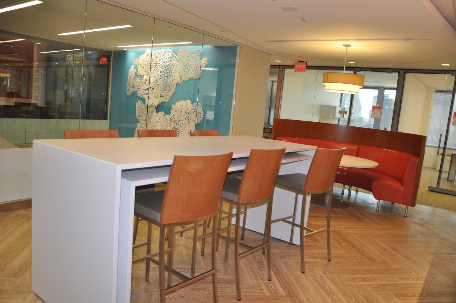 Modern office lounge with high tables, orange stools, and a red curved sofa in a bright lobby