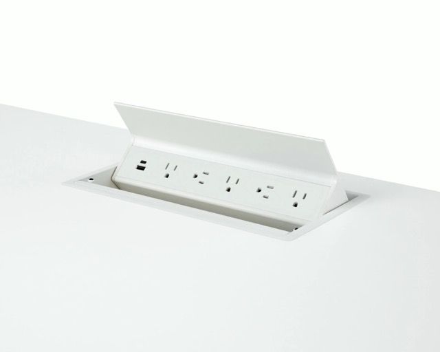 Hand lifting a white pop-up power outlet from a desk surface