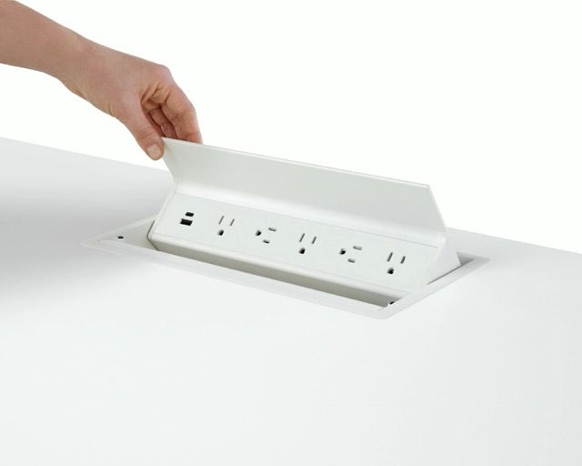 Hand lifting a white pop-up power outlet from a desk surface