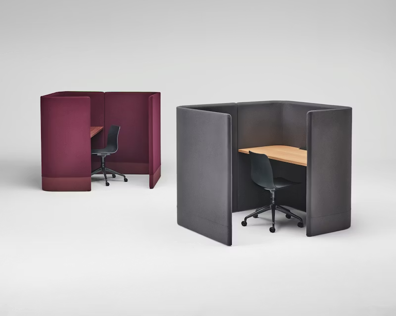 Two small office privacy booths with chairs, one burgundy and one gray, on a white background