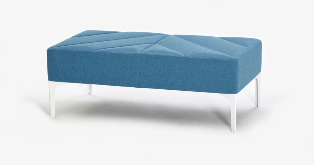 Blue upholstered ottoman with tufted top and white legs on a white background