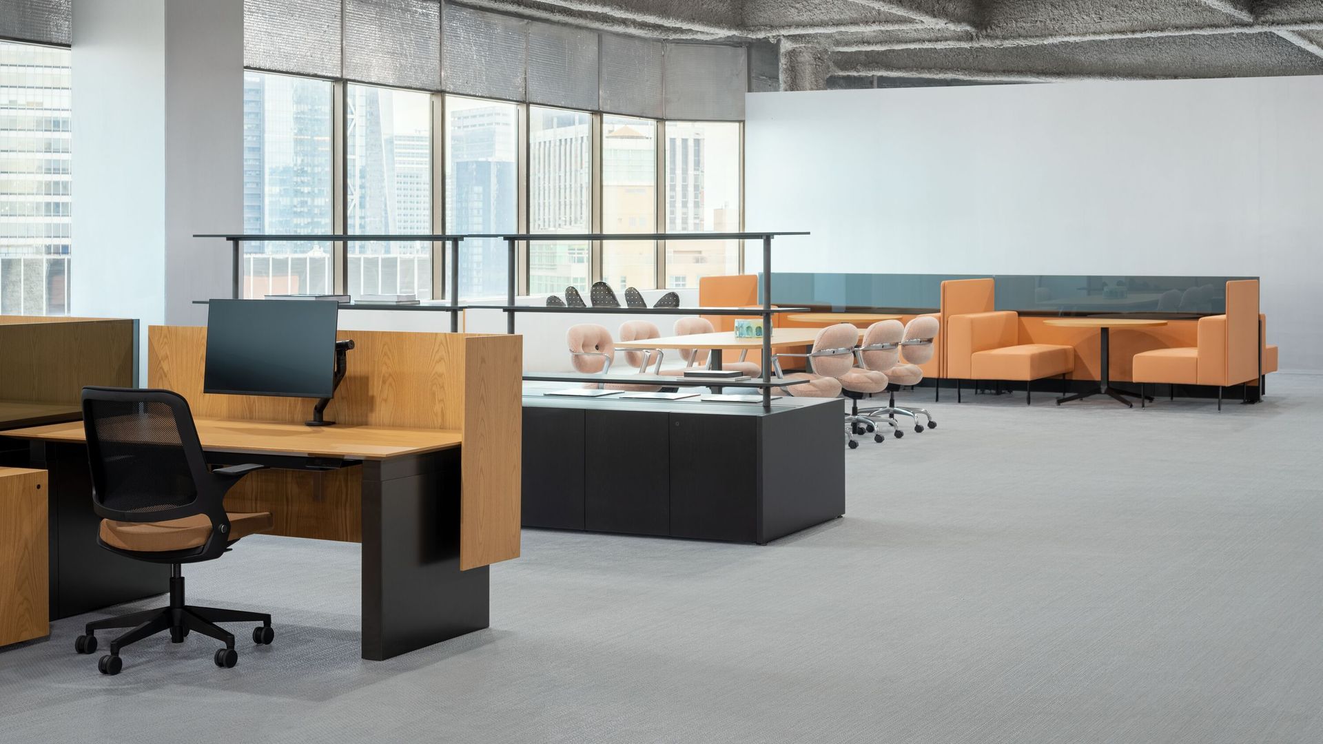Modern office lounge with desks, black chairs, glass dividers, and orange sofas on gray carpet.