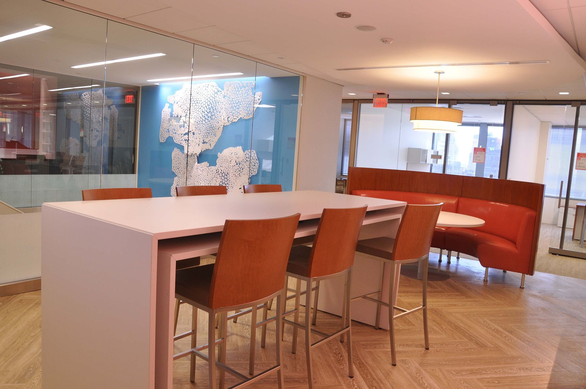 Modern office lounge with white table, orange chairs, and red curved seating behind glass walls