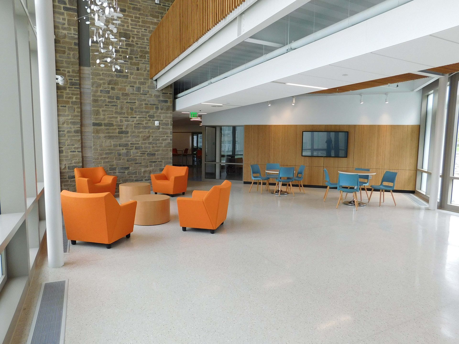 Modern lobby with orange chairs, blue tables, and a high ceiling with wood and brick accents