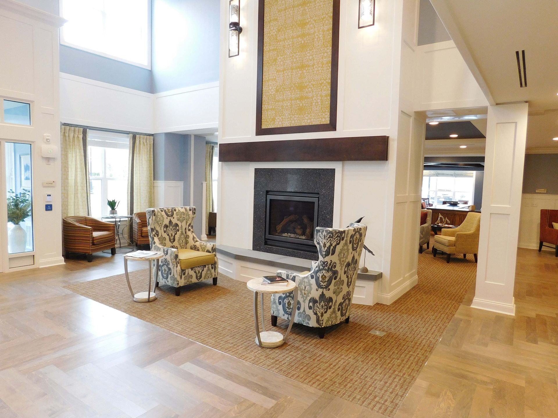 Bright living room with fireplace, wicker chairs, and light wood floors, viewed from an open hallway