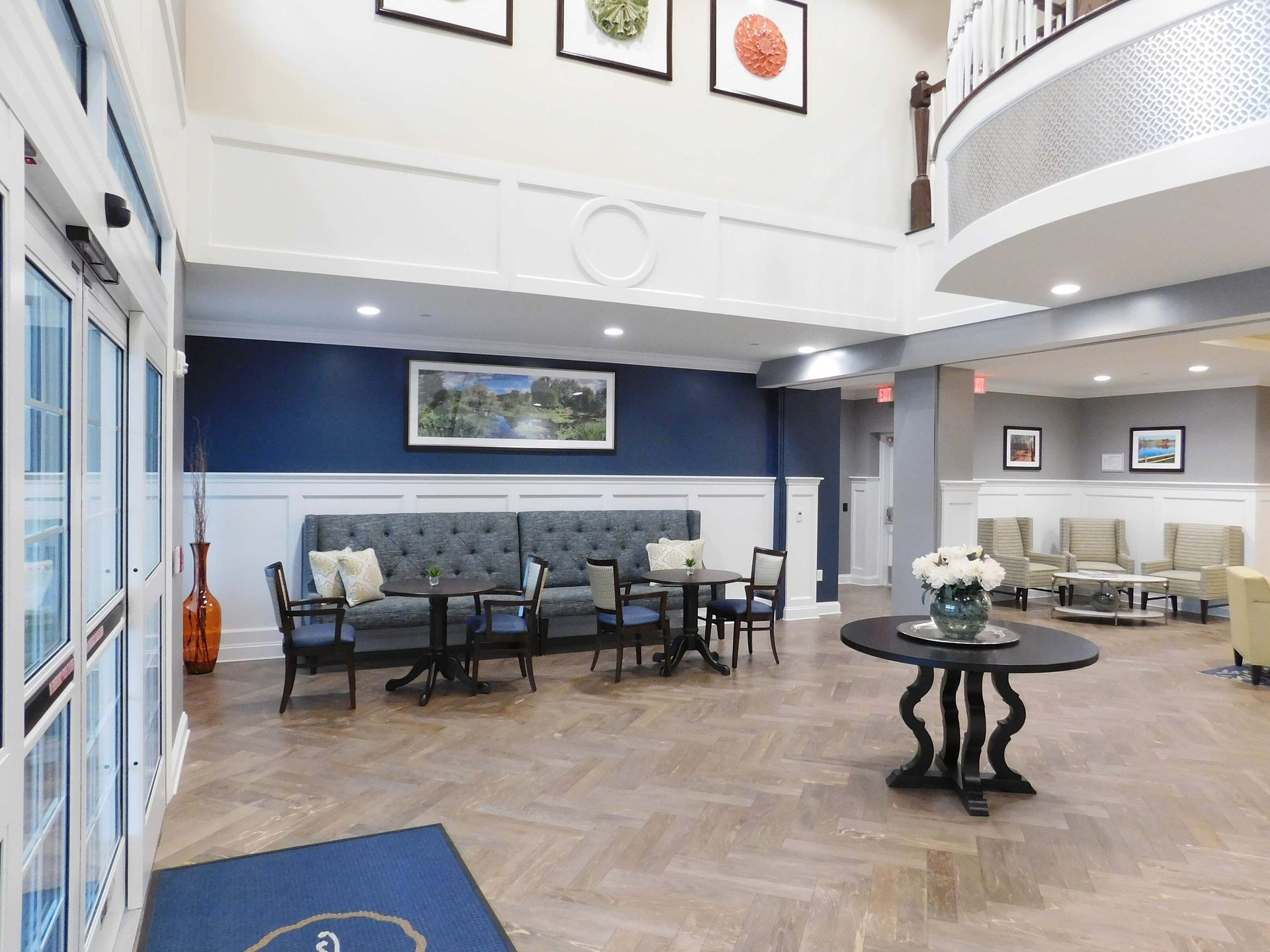 Bright lobby with blue walls, seating areas, and a central round table beneath high ceilings.