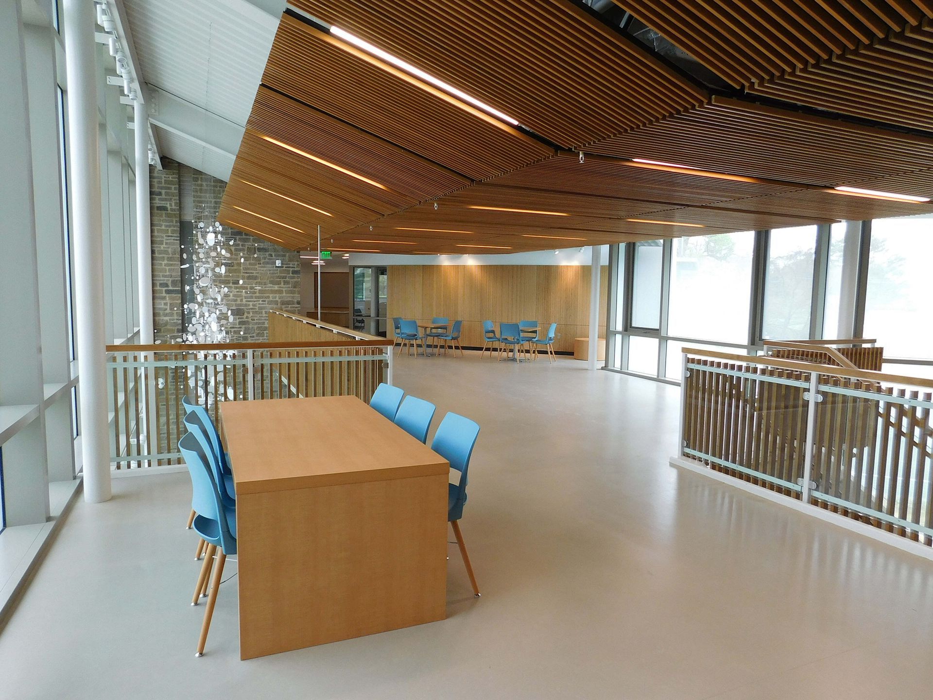 Modern lounge with wooden table, blue chairs, and curved wood ceiling beside large windows