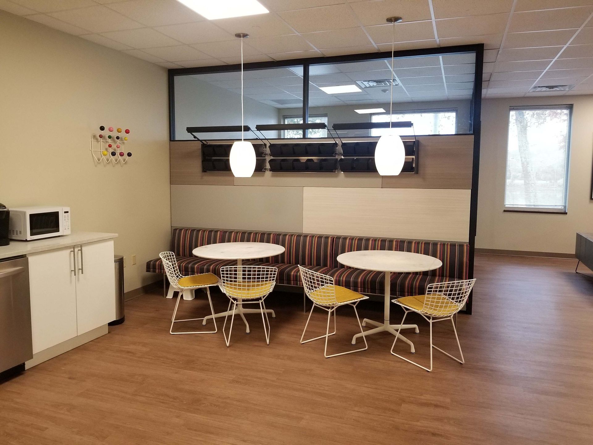 Small break room with round tables, yellow chairs, kitchenette, and large interior window￼