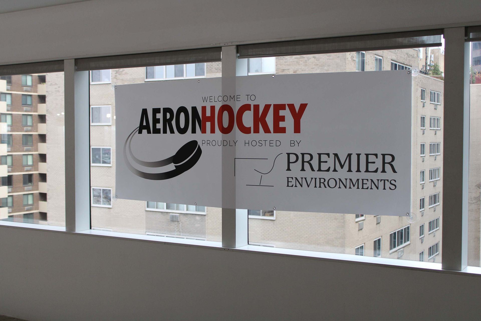AERONHockey and Premier Environments signs on a window with city buildings outside