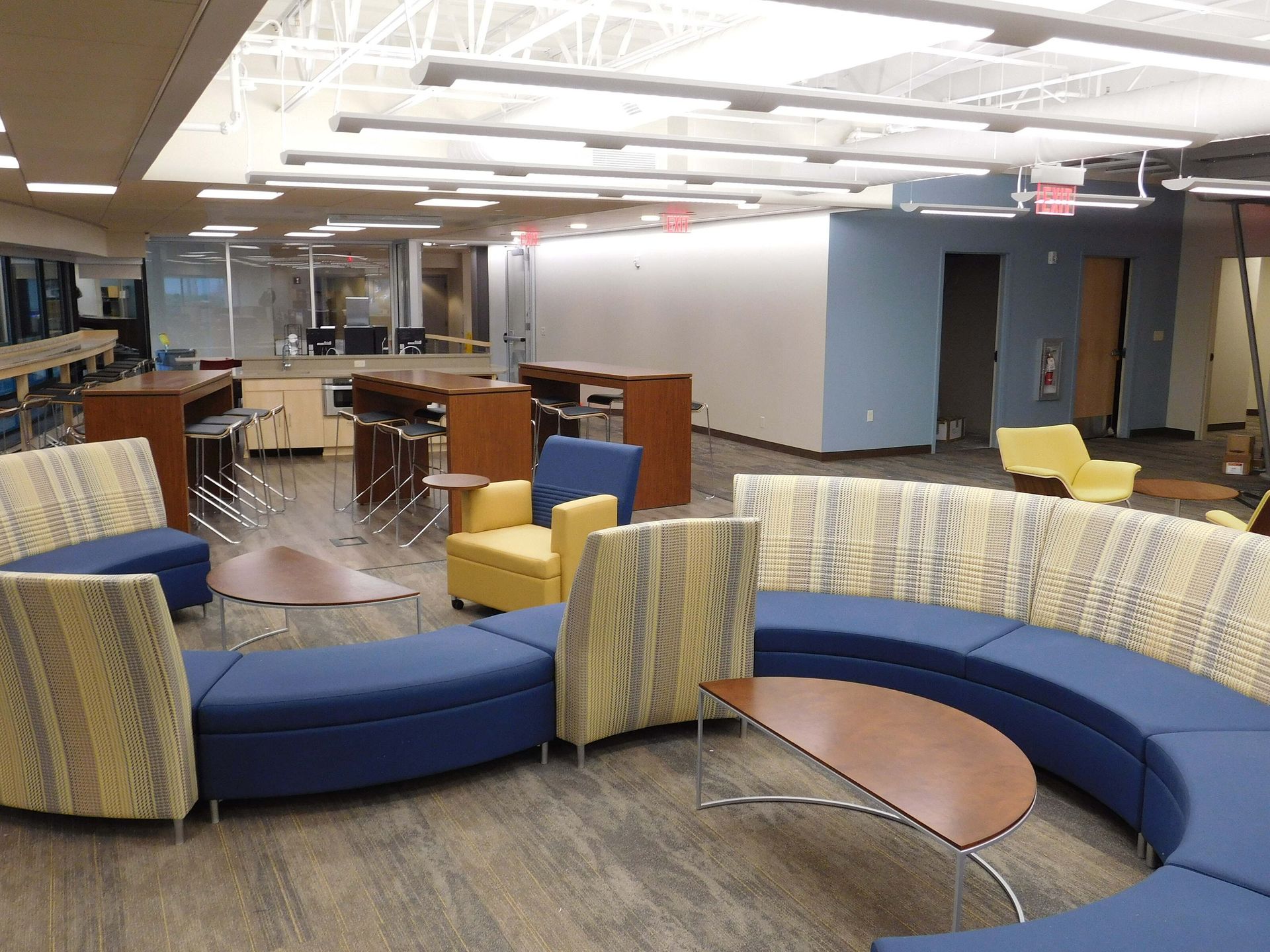 Modern library lounge with curved blue seating, small tables, and bookshelves under bright ceiling lights