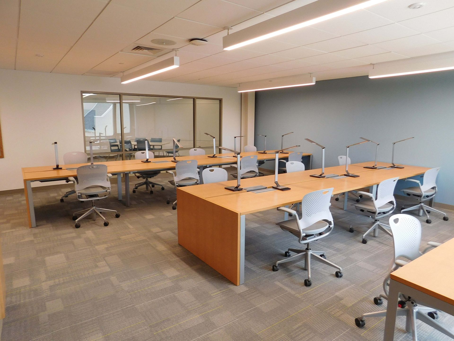 Empty office conference room with desks, swivel chairs, and glass-walled meeting area