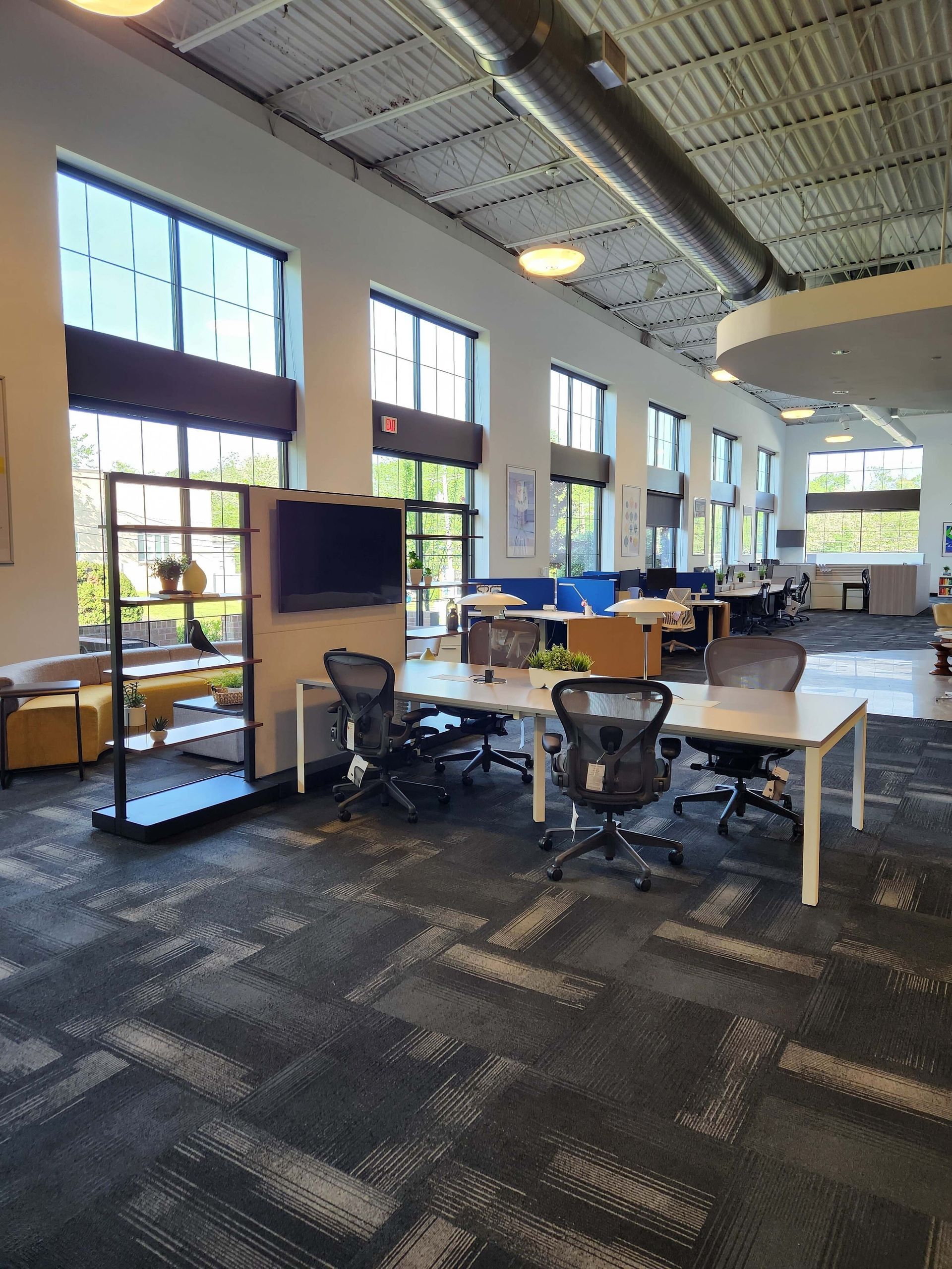 Modern office lounge with desks, chairs, TV, and large windows in an open workspace