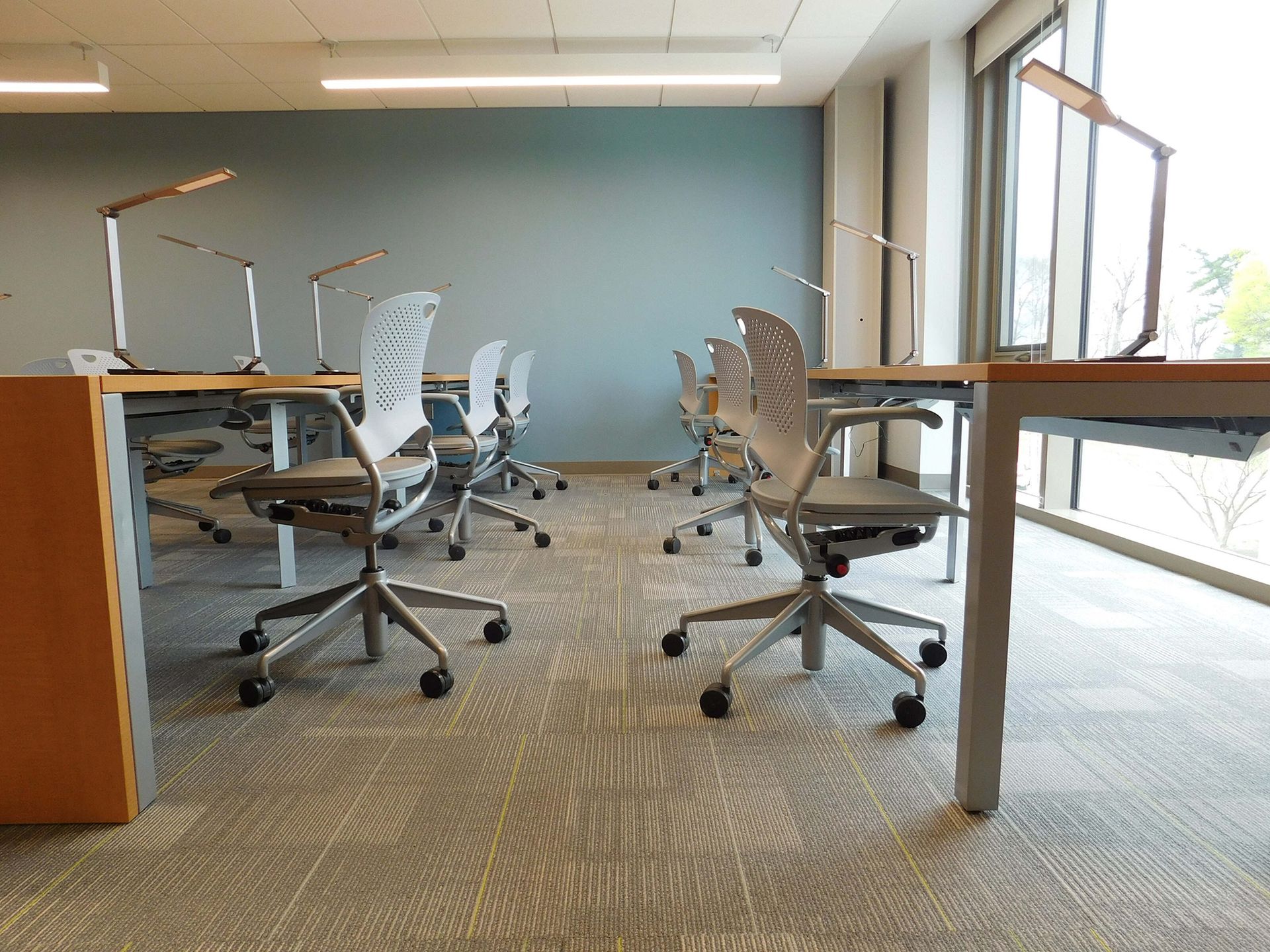 Empty modern office with rolling chairs, desks, and large windows with daylight.