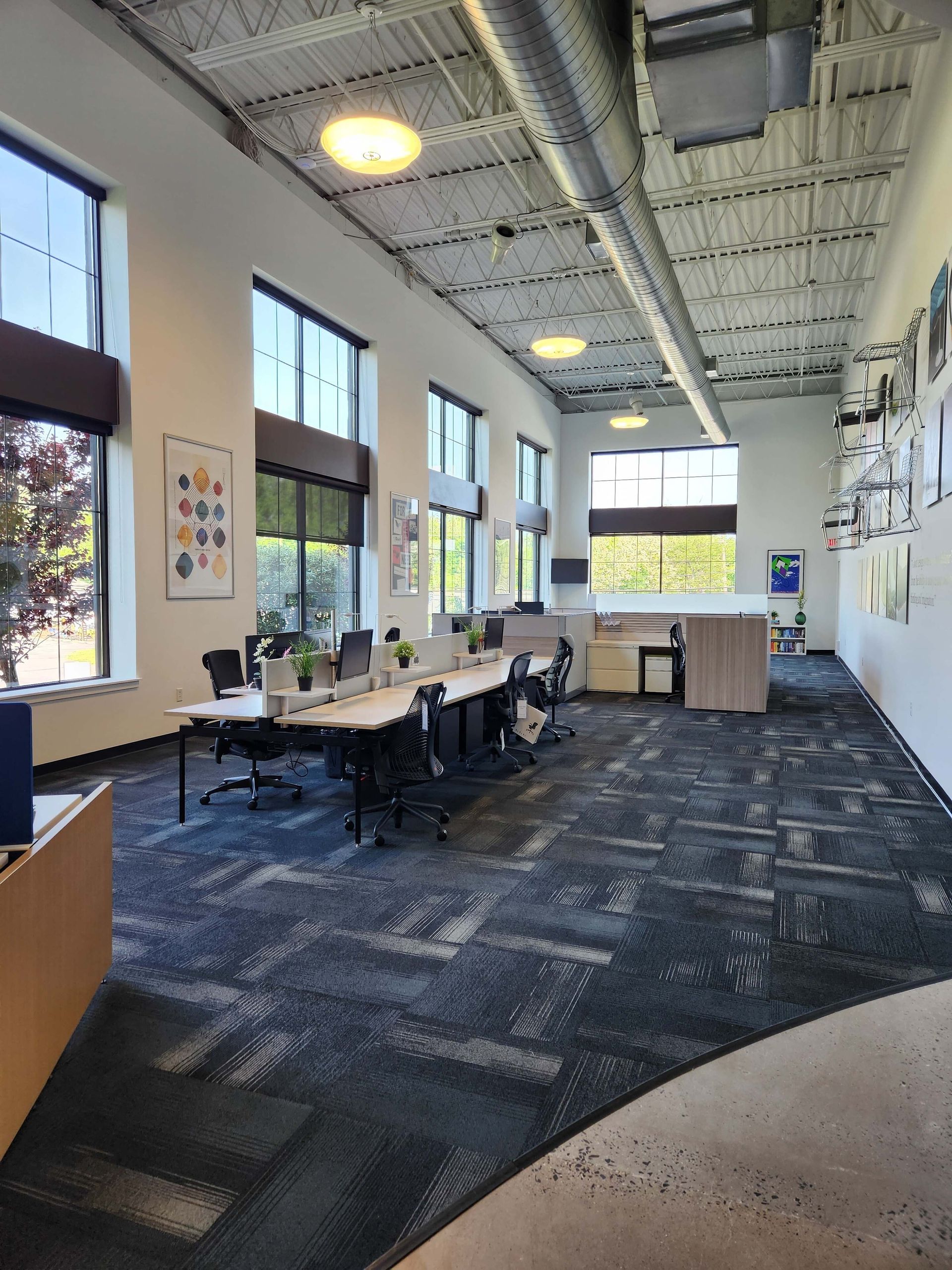 Modern office lounge with tables, chairs, tall windows, and patterned carpet under bright ceiling lights