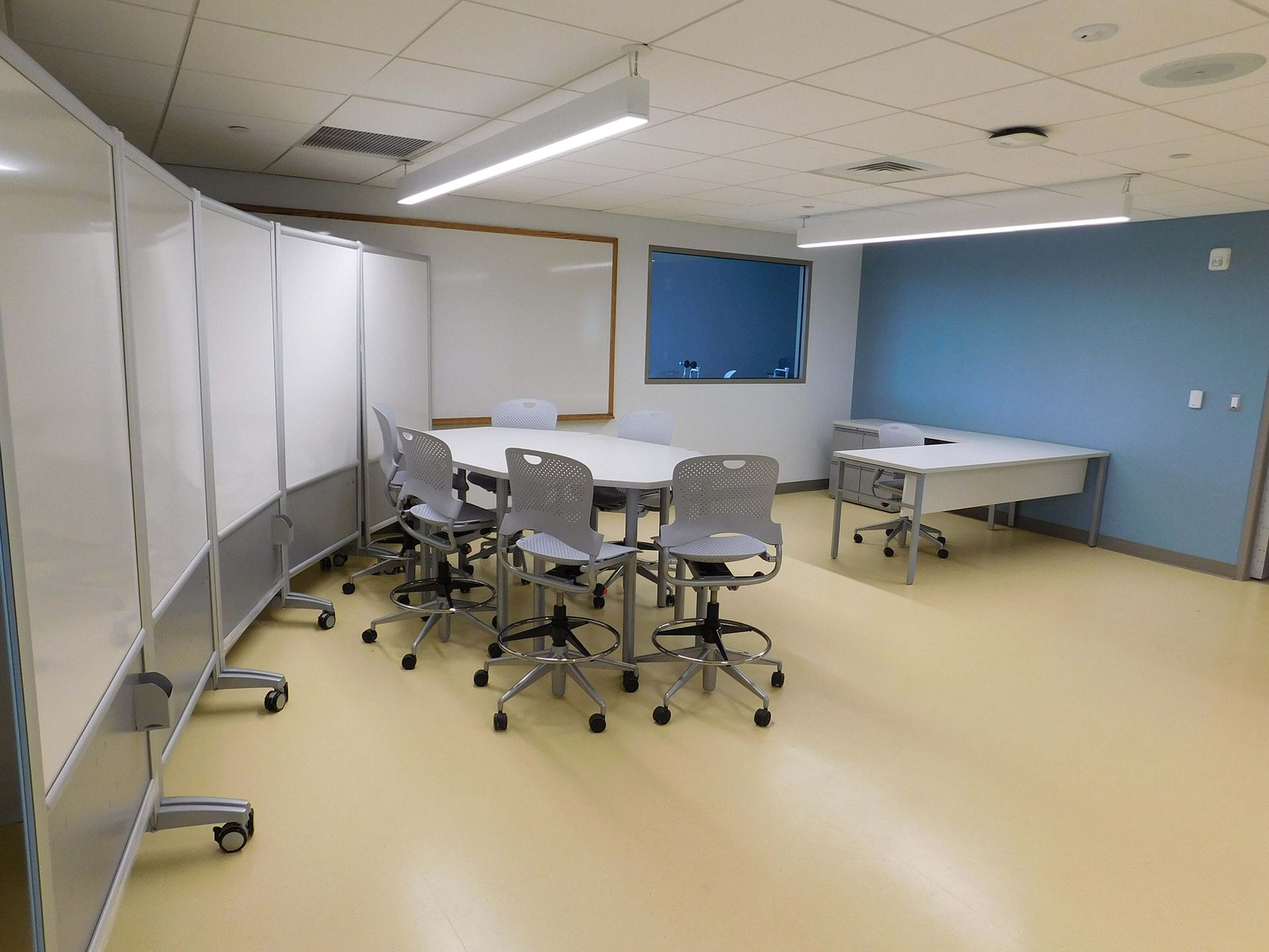Conference room with tables and rolling chairs, white dividers, and blue walls.