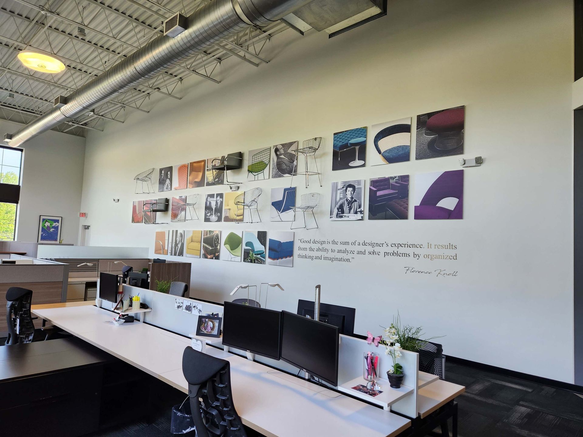 Modern office with long desks, computer monitors, and a white wall covered in colorful design sketches.