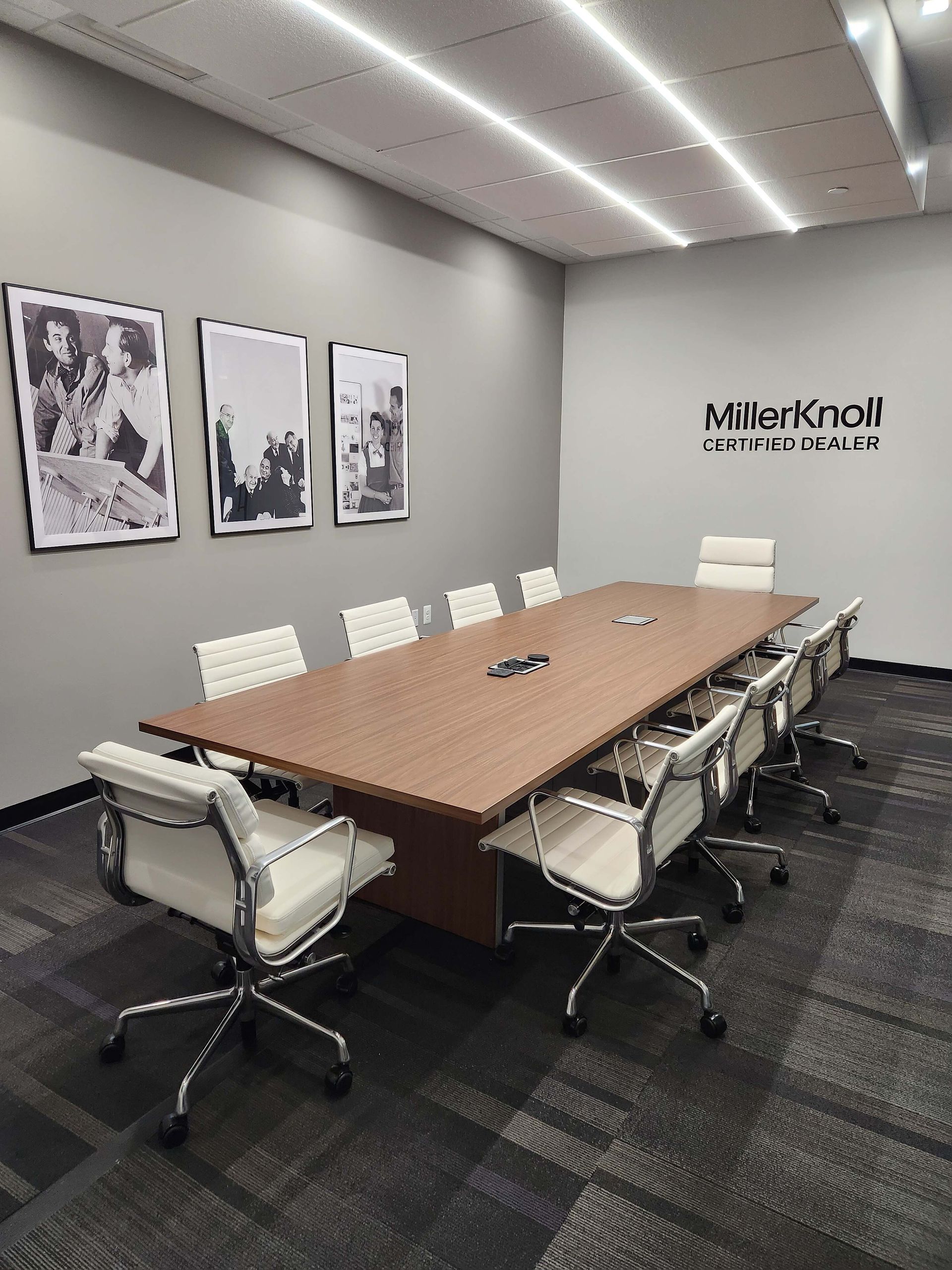 Modern conference room with long wooden table, white chairs, wall art, and logo on the far wall