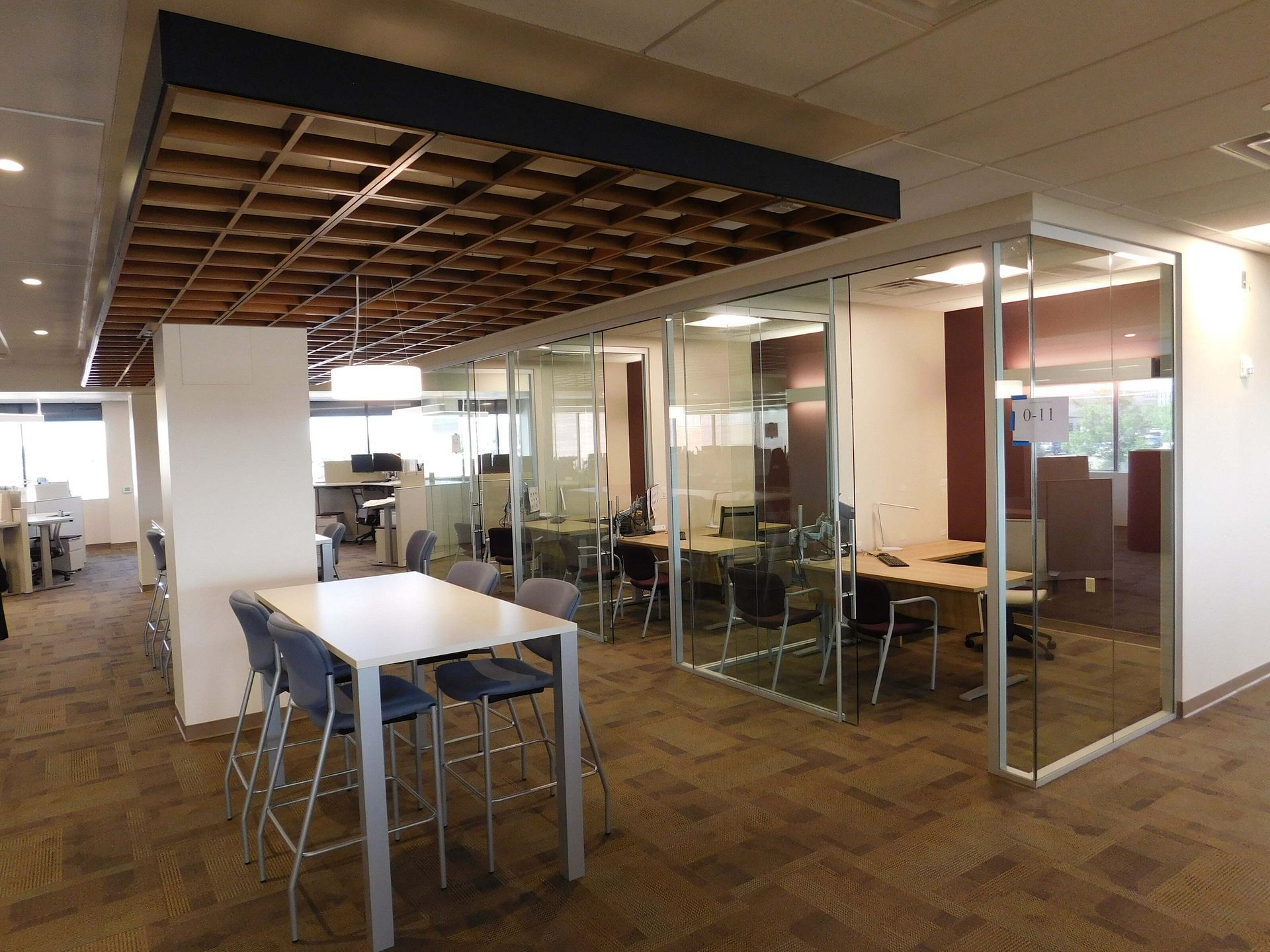 Modern office lounge with glass-walled meeting rooms and tables under an exposed ceiling
