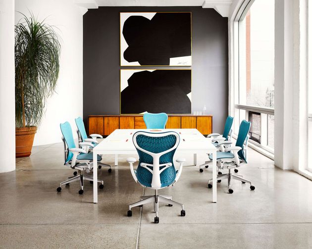 Modern conference room with white table, blue chairs, orange bench, and large window view