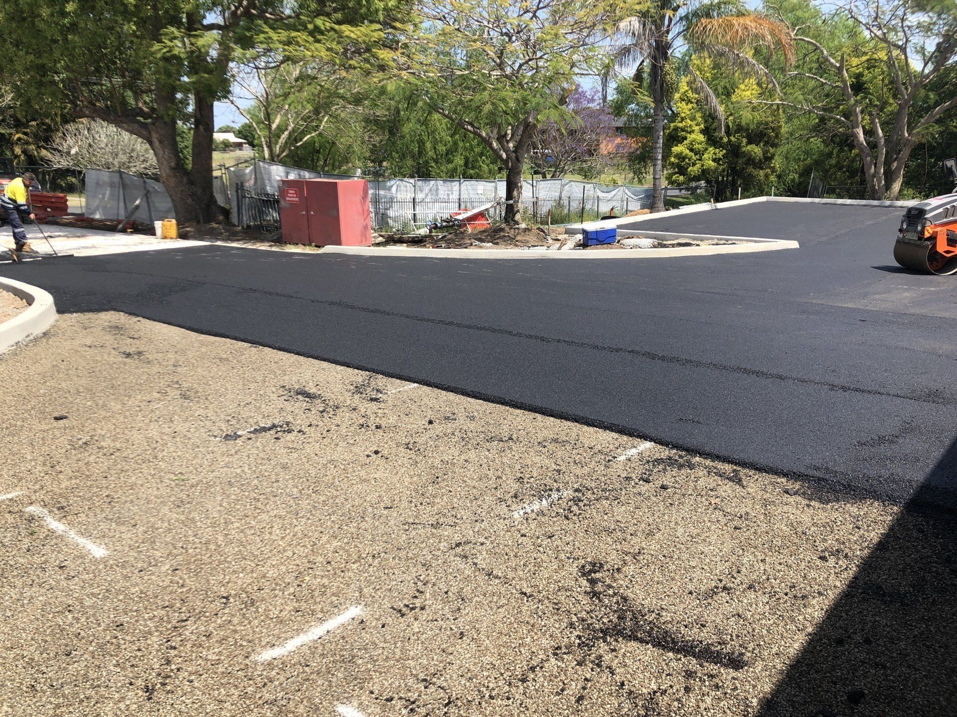 A roller is rolling asphalt in a parking lot.