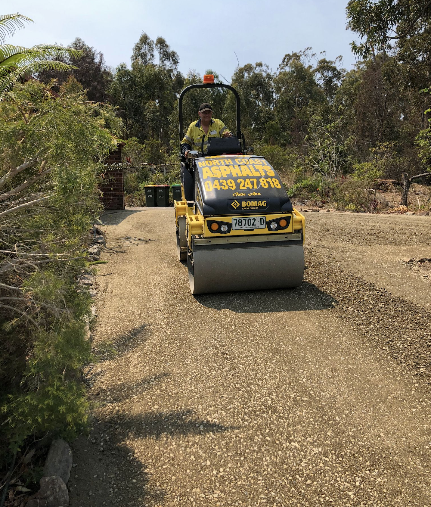A man is driving a yellow roller on a gravel road.