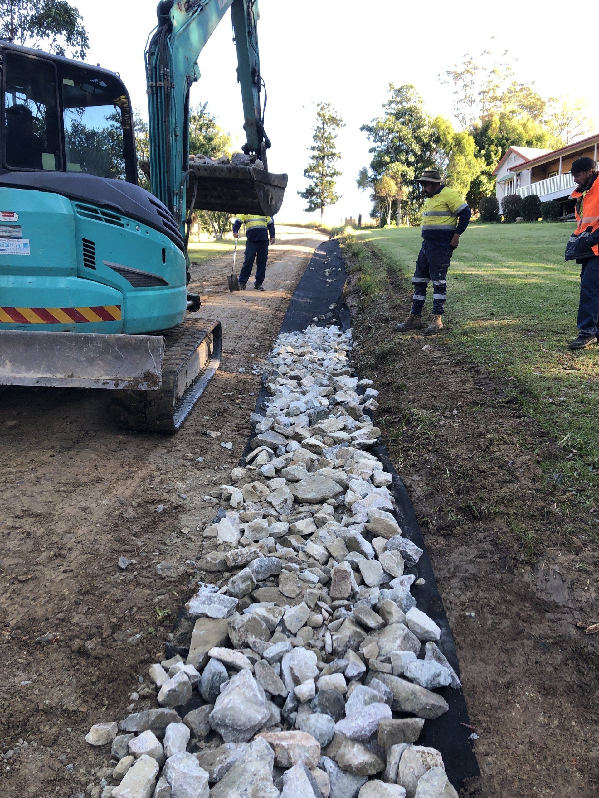 A man is standing next to a pile of rocks next to a construction vehicle.