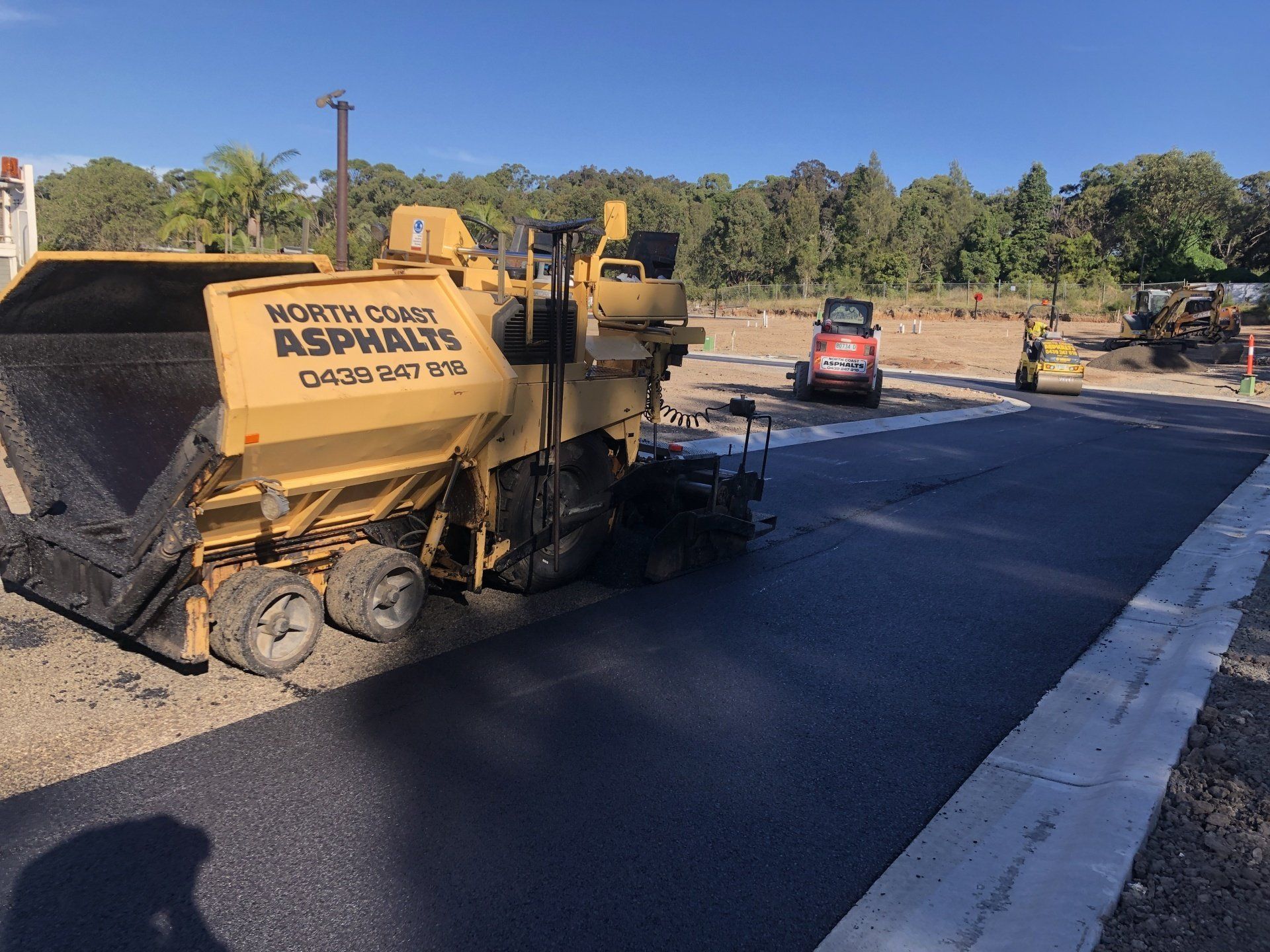 A yellow asphalt paving machine is working on a road.