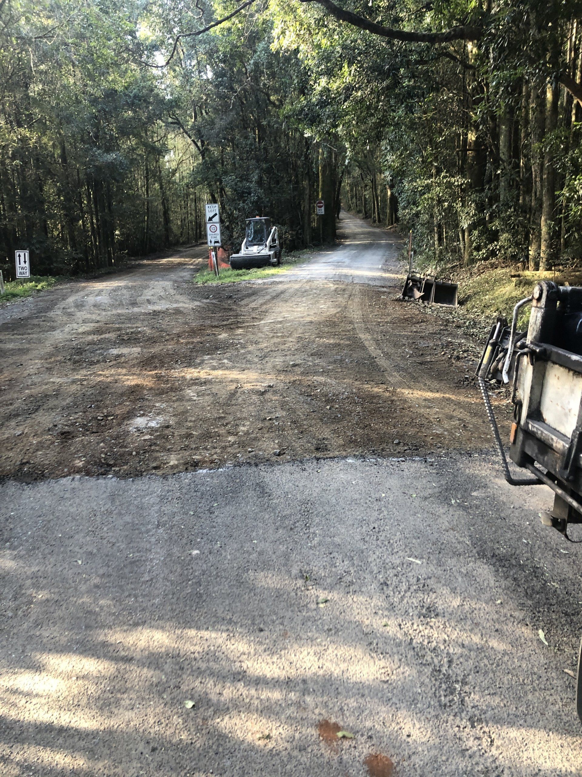 A truck is parked on the side of a dirt road in the woods.