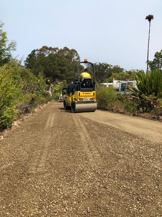 A yellow roller is rolling gravel on a dirt road.