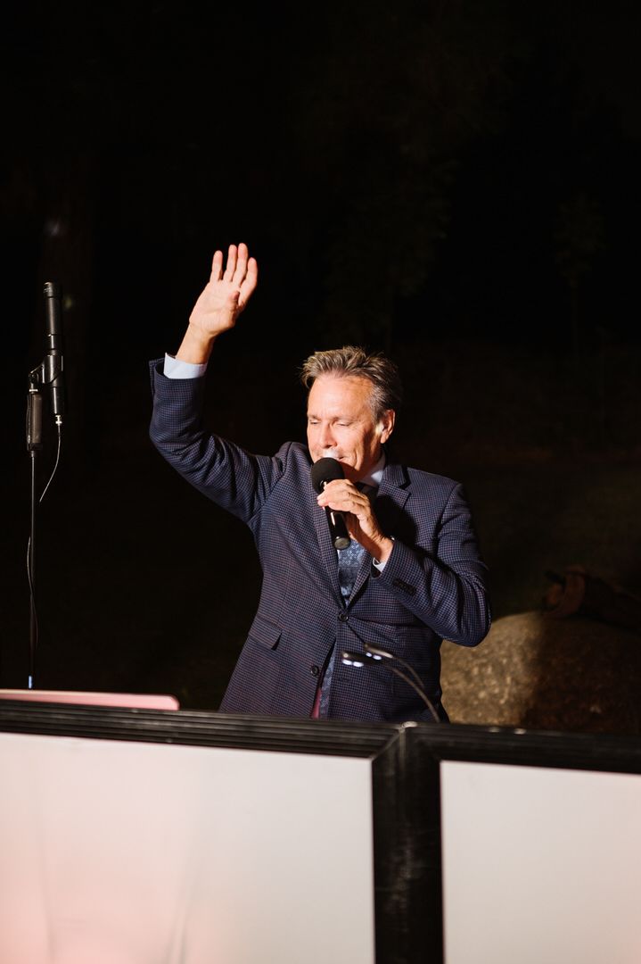 A man in a suit is standing in front of a microphone and waving his hand.