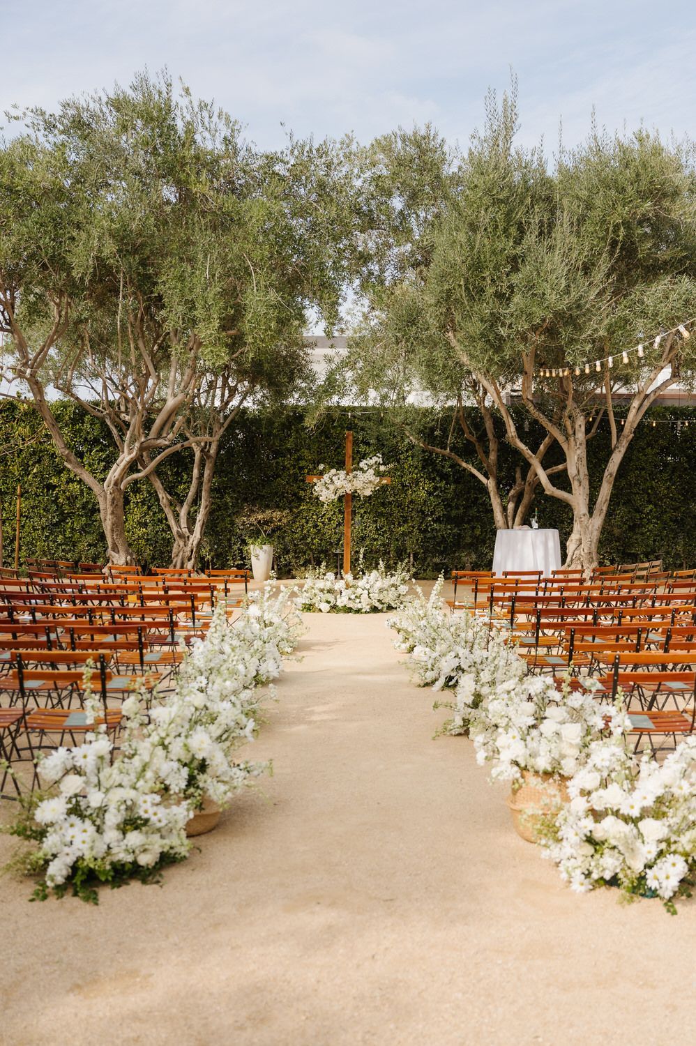 A row of wooden chairs lined up along a aisle decorated with white flowers.