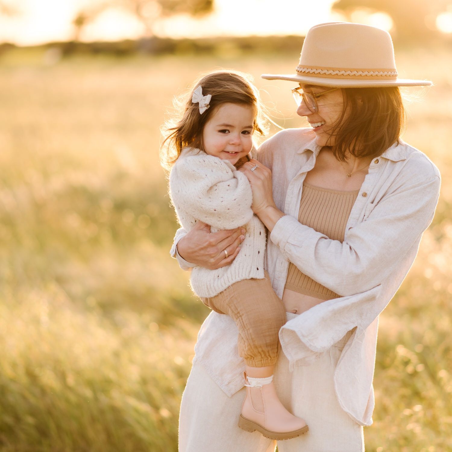 A woman in a hat is holding a little girl in her arms in a field.
