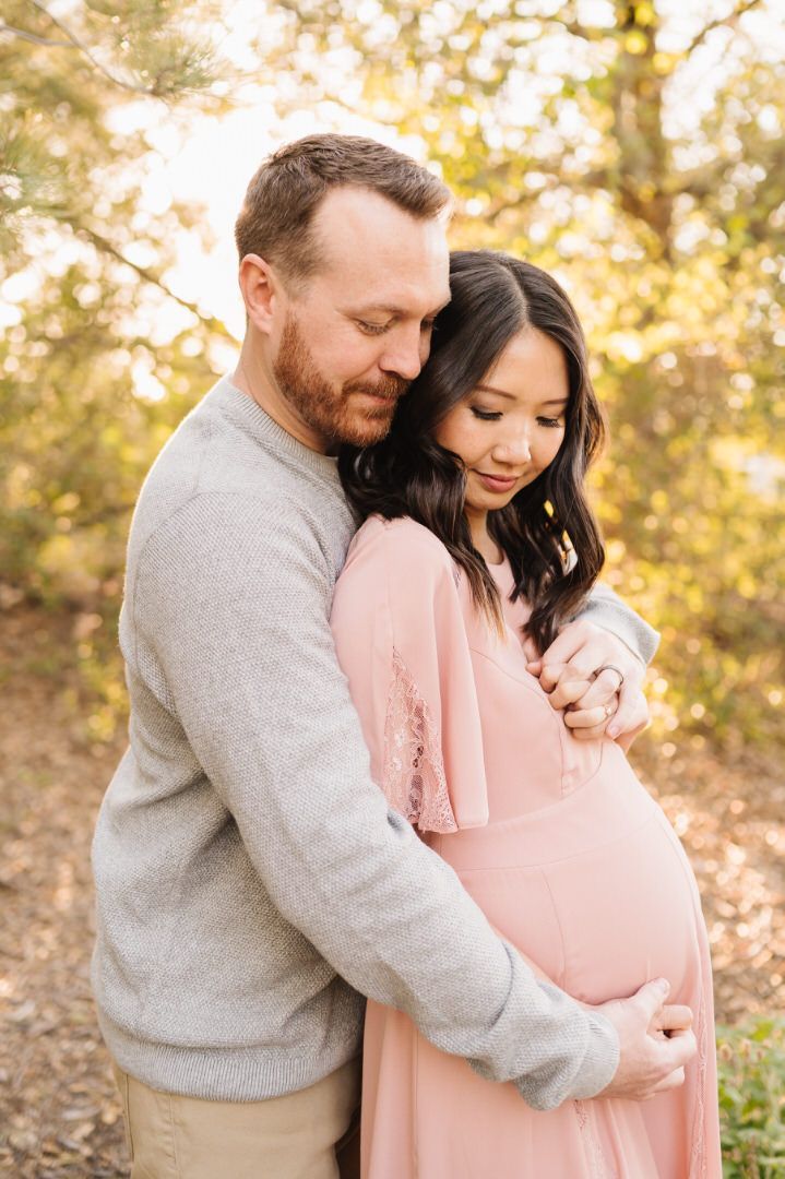 A man is hugging a pregnant woman in a pink dress.