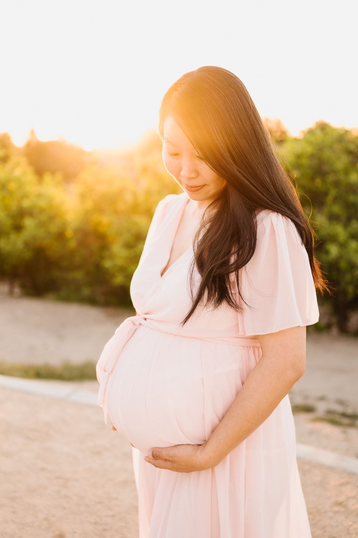 A pregnant woman in a pink dress is holding her belly.