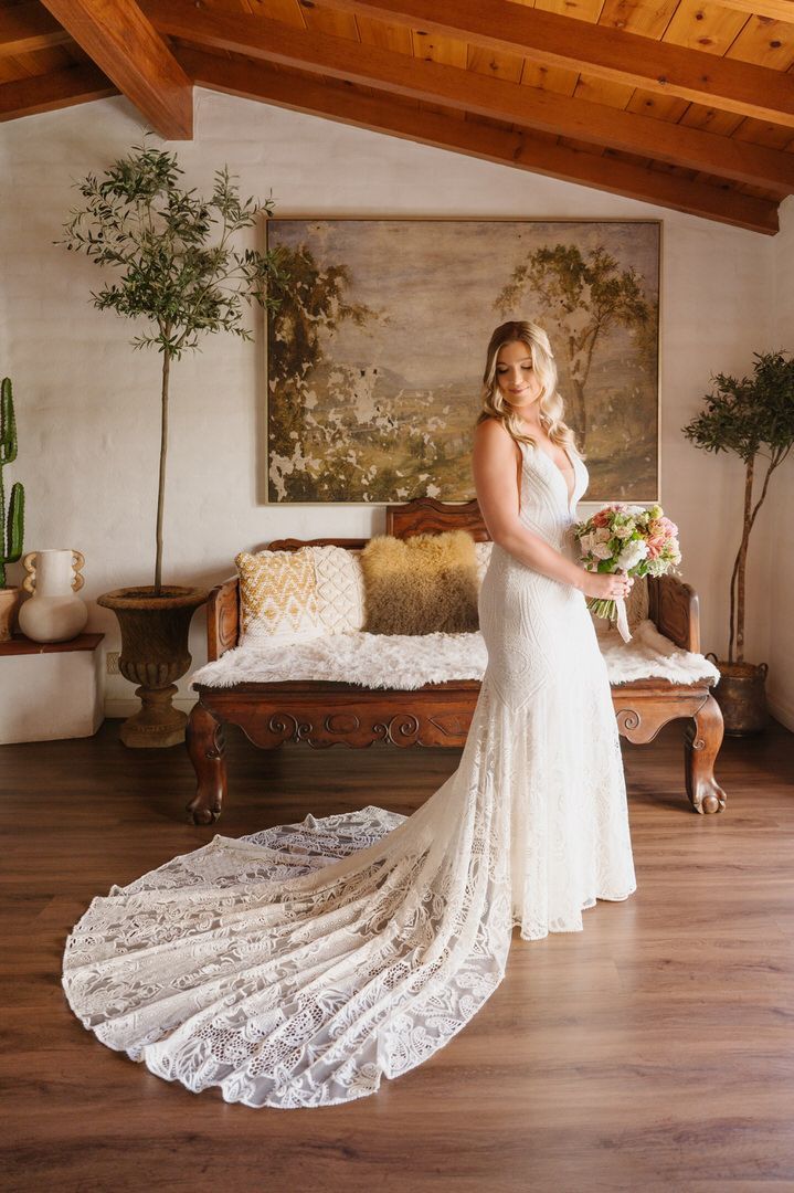 A woman in a wedding dress is standing in a room holding a bouquet of flowers.