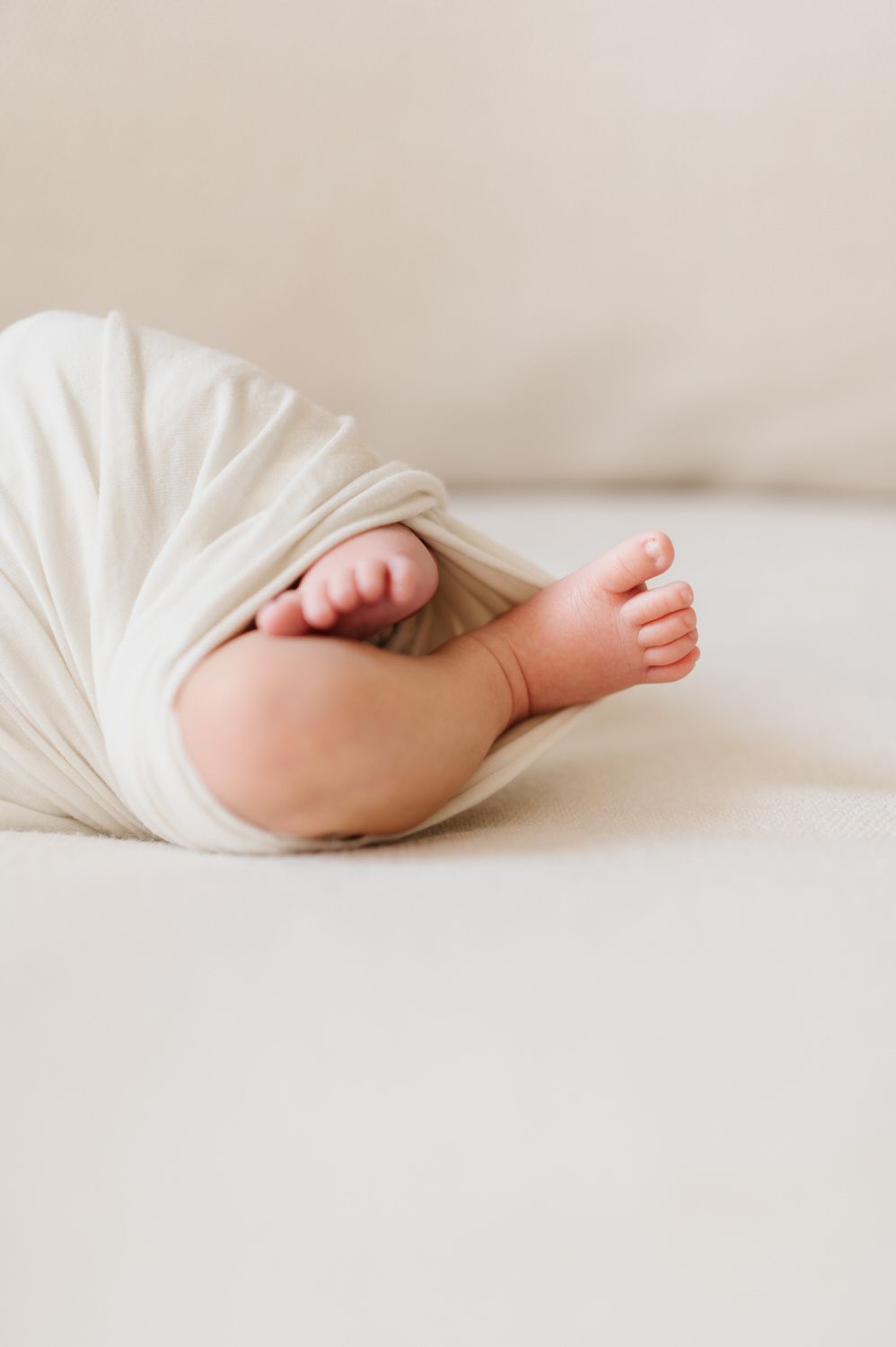 A newborn baby wrapped in a white blanket is laying on a bed  for an in home newborn photo in Orange County.