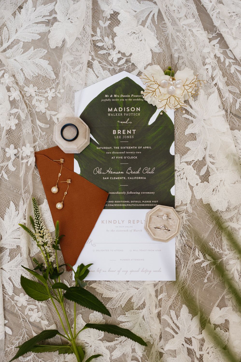 A wedding invitation is sitting on a table next to flowers and a ring.