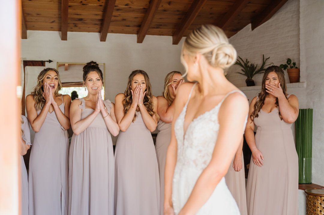 A bride and her bridesmaids are looking at each other in a room.