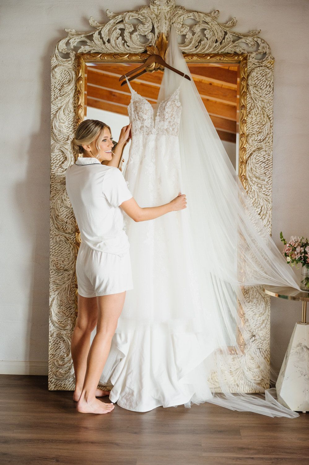 A woman is holding a wedding dress in front of a mirror.