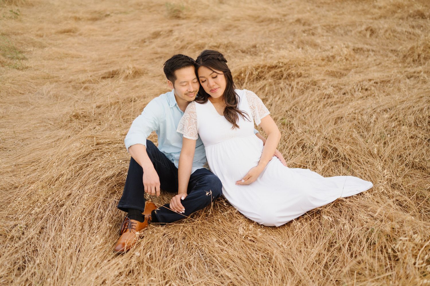 A man and a pregnant woman are sitting on the ground in a field.