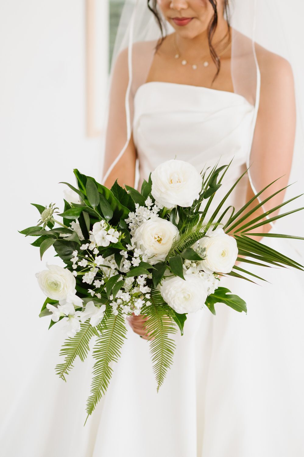 A bride in a white dress is holding a bouquet of white flowers.