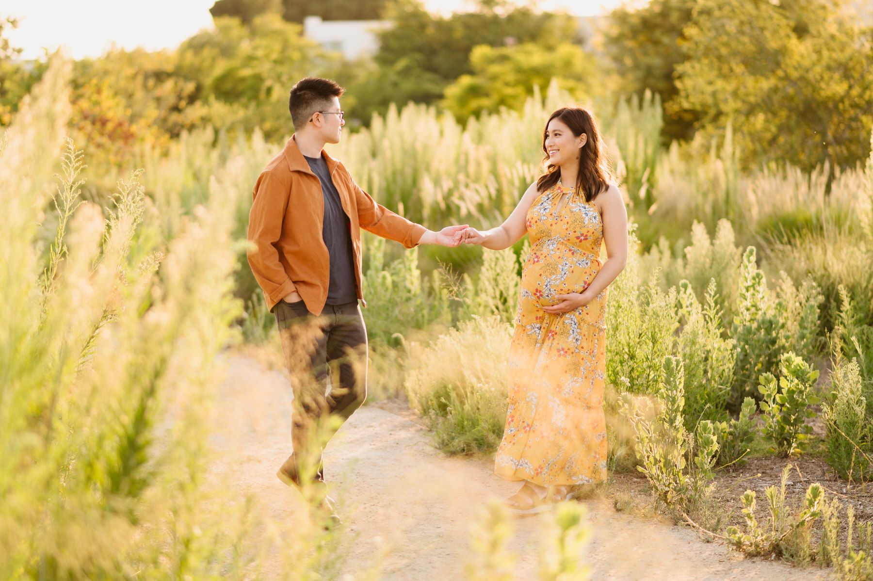 A man and a pregnant woman are holding hands in a field.
