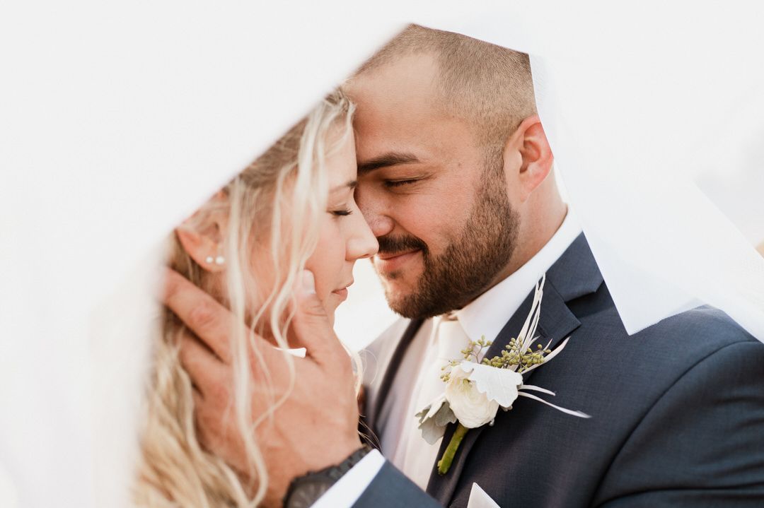 A bride and groom are looking into each other 's eyes under a white veil.