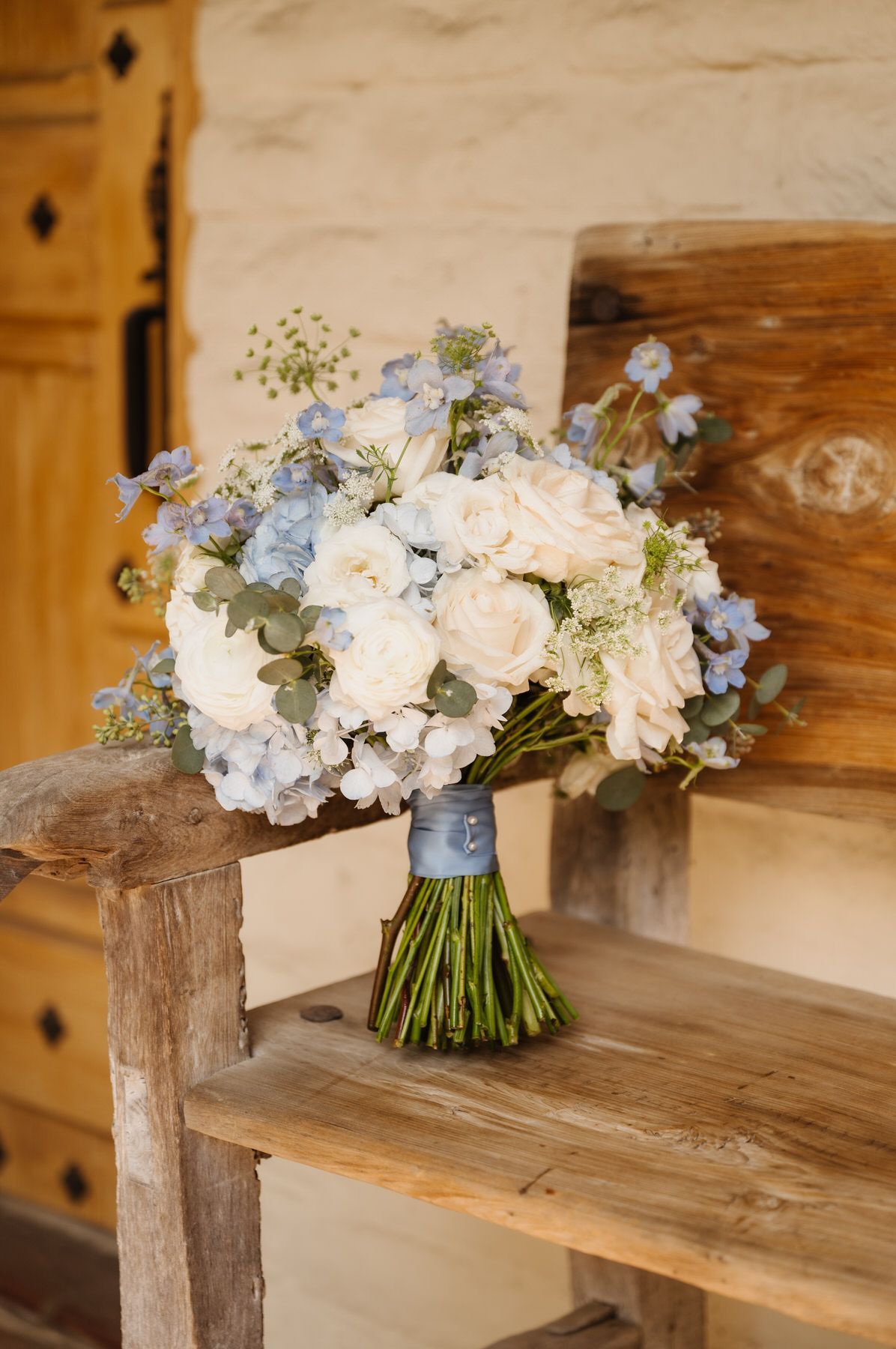 A bouquet of white and blue flowers is sitting on a wooden bench.