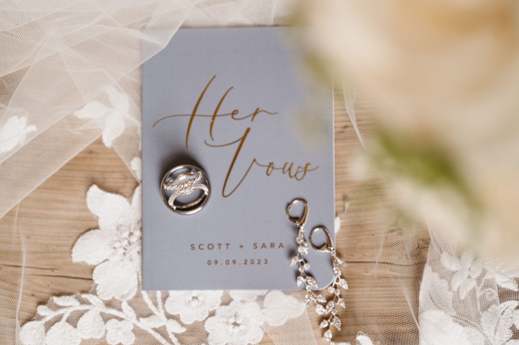A bride and groom 's wedding rings are on a card on a wooden table.