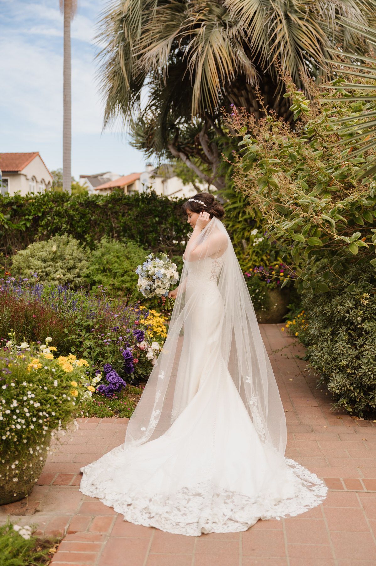 A bride in a wedding dress and veil is standing in a garden.