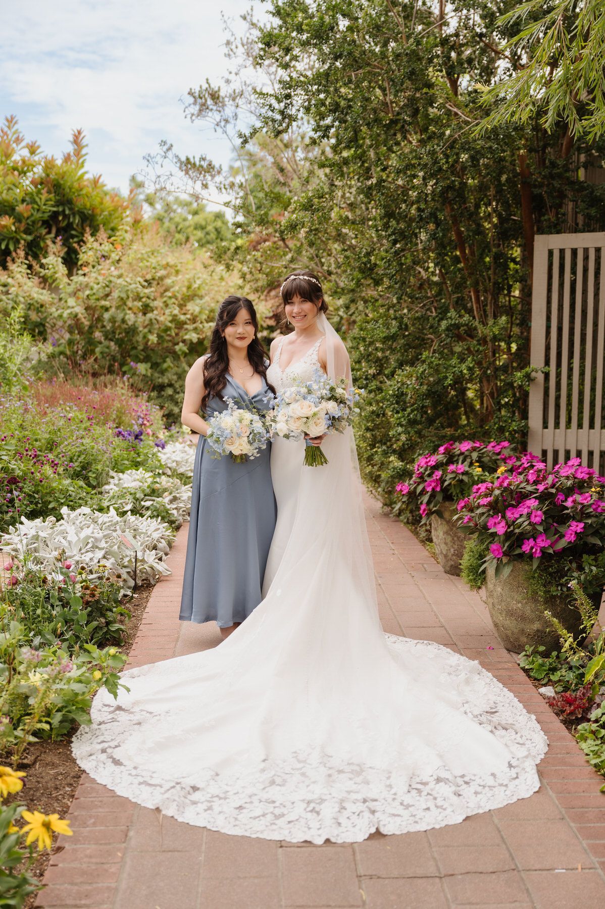 A bride and her bridesmaid are posing for a picture in a garden.